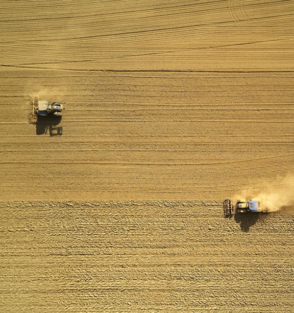 Aerial view of two tractors working in a large, golden wheat field.